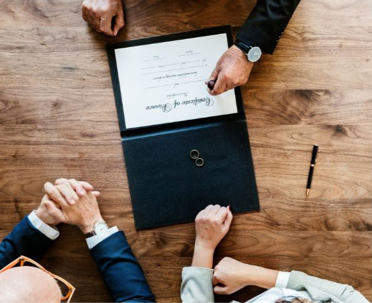 Divorce paperwork being signed at a table with a couple and an attorney, with wedding rings placed on the document nearby