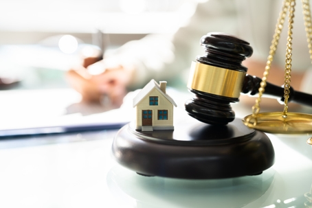 house figure and gavel with someone signing documents in the background